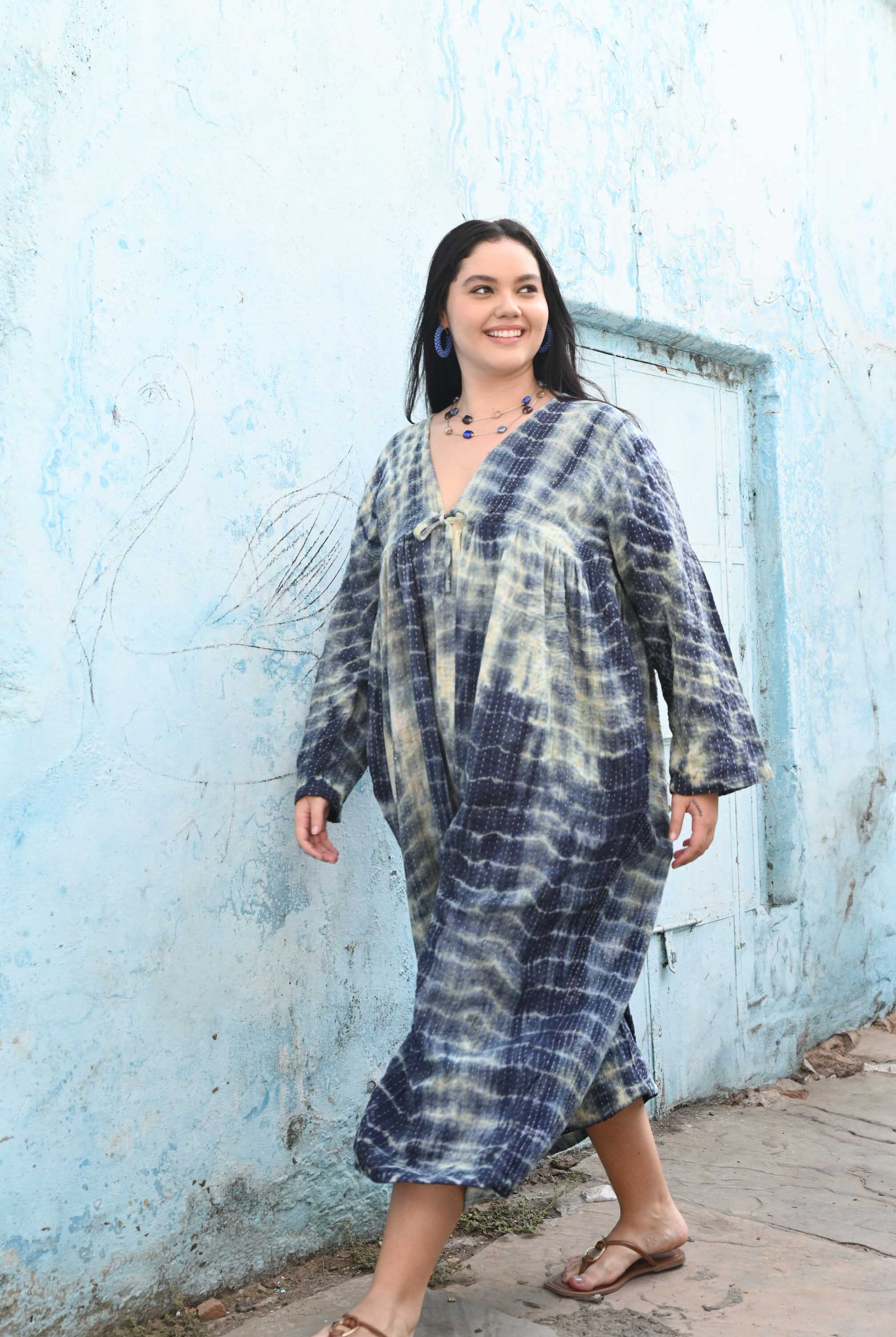 Woman wearing a tie-dye dress standing in front of a blue wall.
