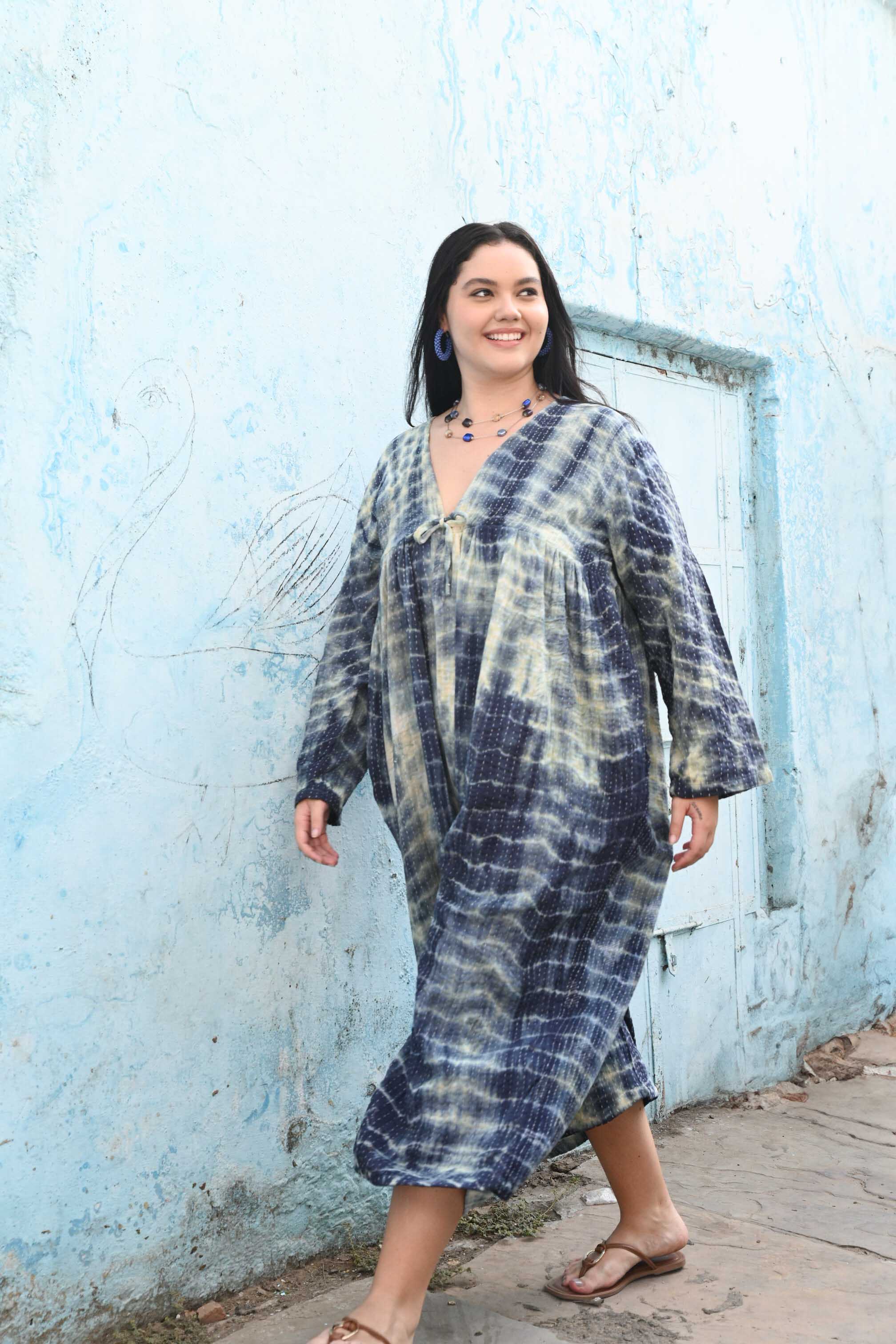 Woman wearing a tie-dye dress standing in front of a blue wall.