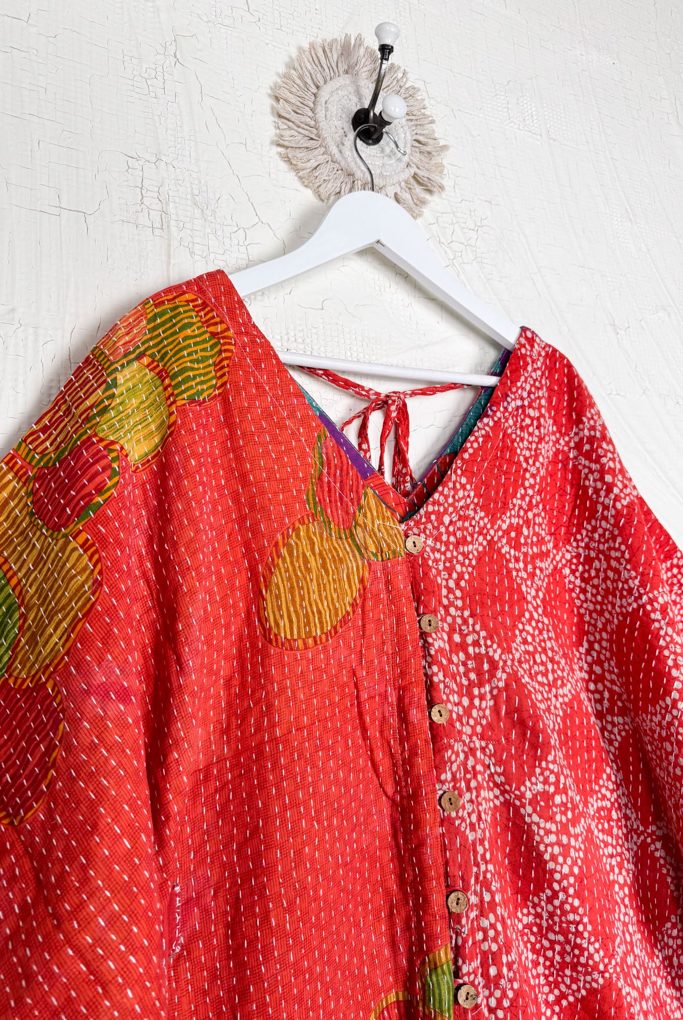 Two red patterned tops hanging on a white hanger against a white wall Lover Protect Sustain