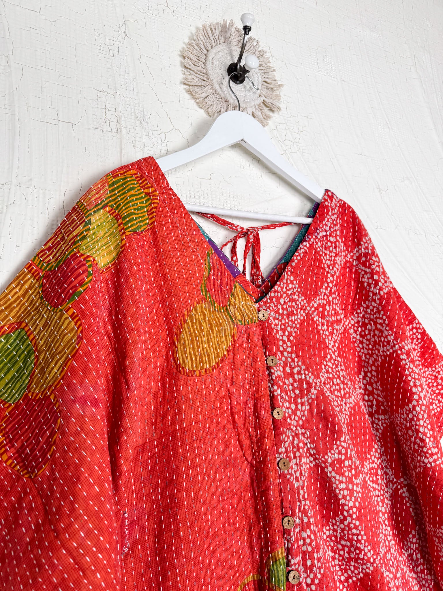 Two red patterned tops hanging on a white hanger against a white wall Lover Protect Sustain
