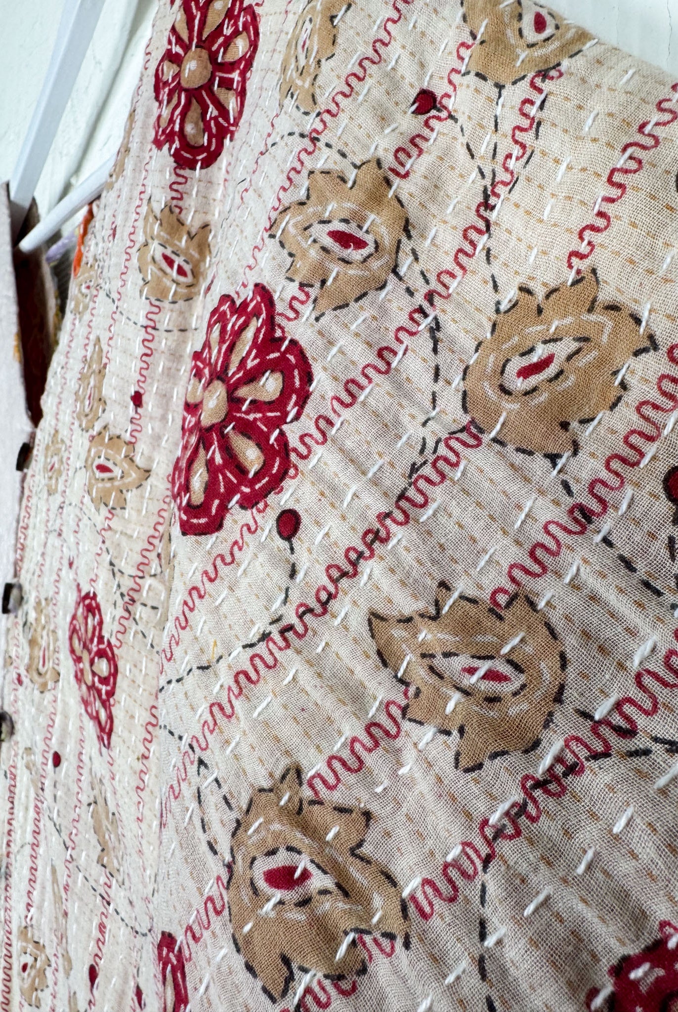 Close-up of a textured fabric with floral patterns in red and brown on a beige background.