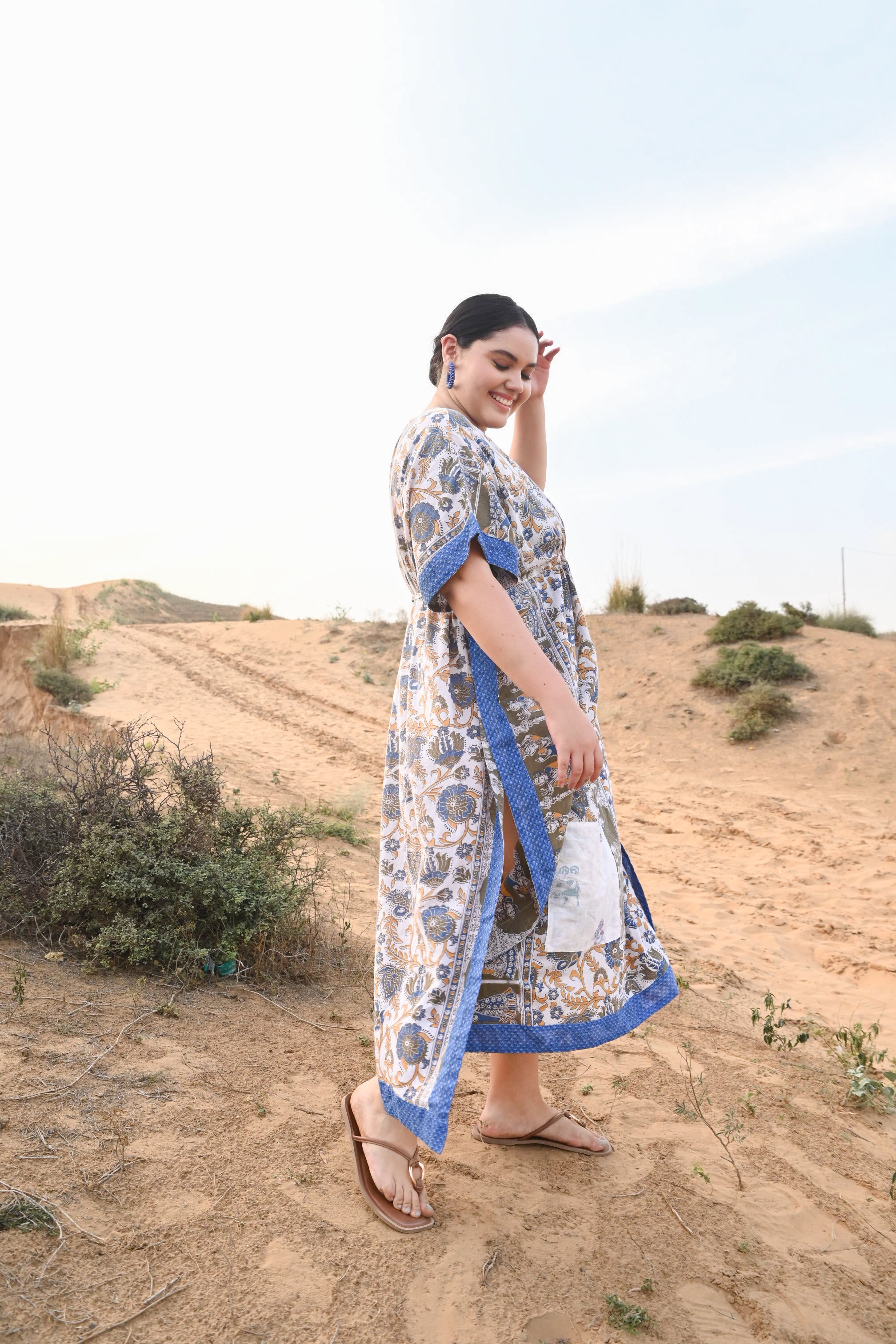 Woman in a floral dress with blue trim standing in a desert landscape - Love Protect Sustain