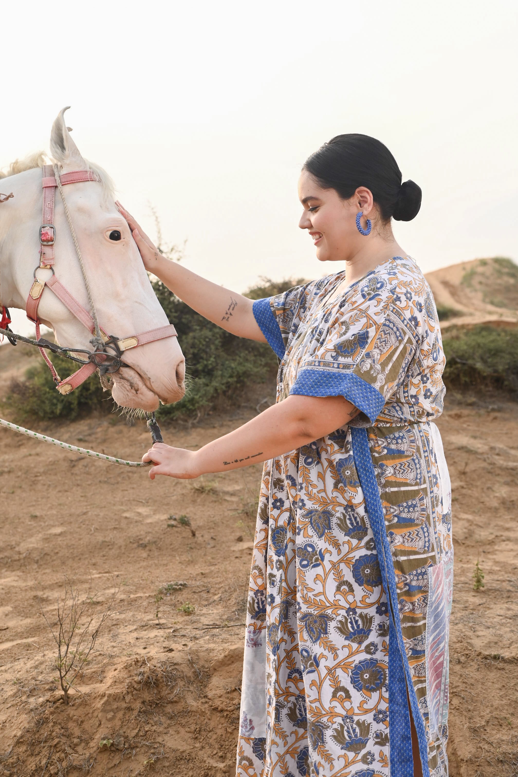 Woman in a patterned dress standing next to a horse in an outdoor setting - Love Protect Sustain