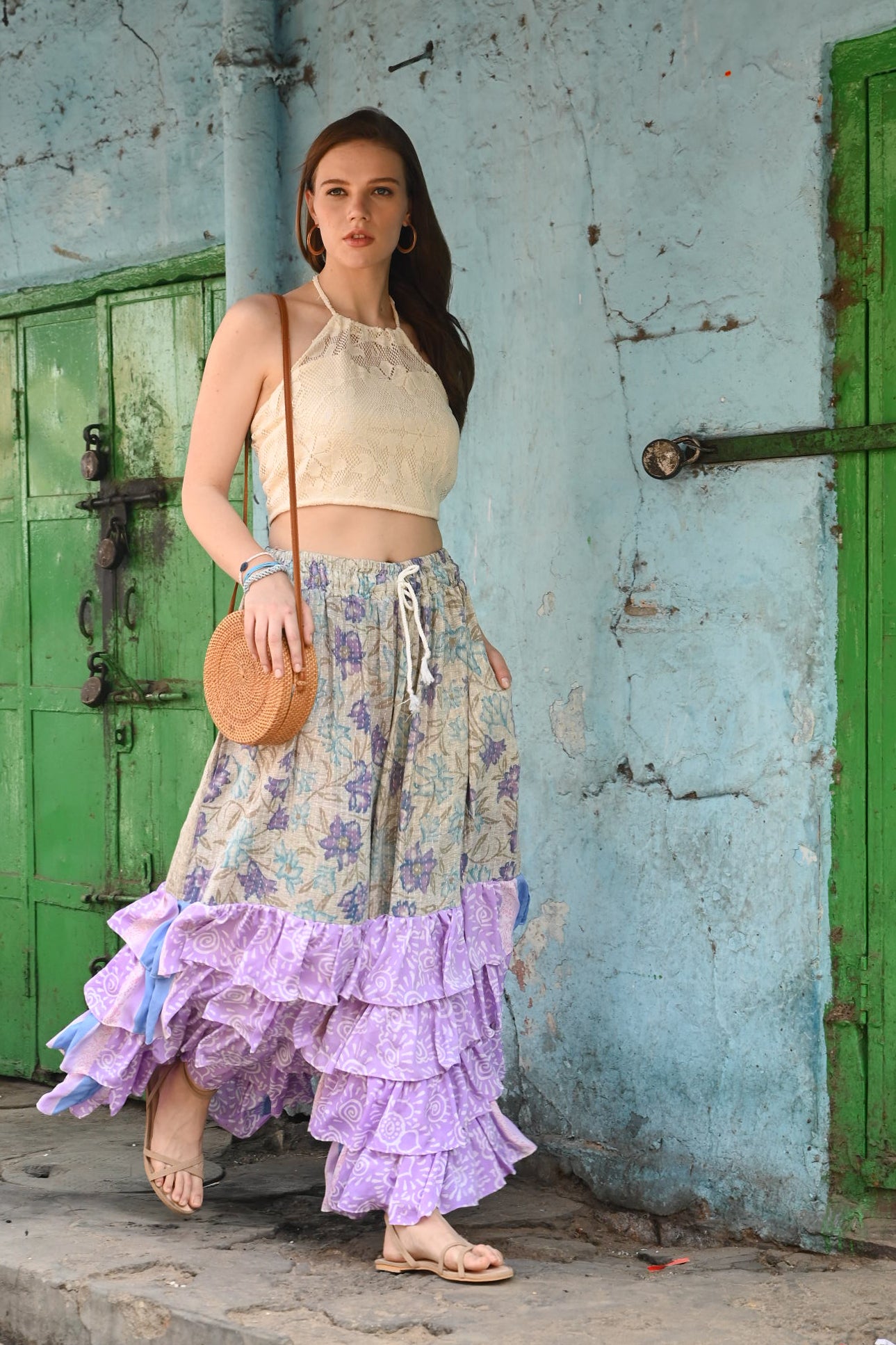 Woman in a floral dress with ruffled layers standing against a textured wall with green doors.