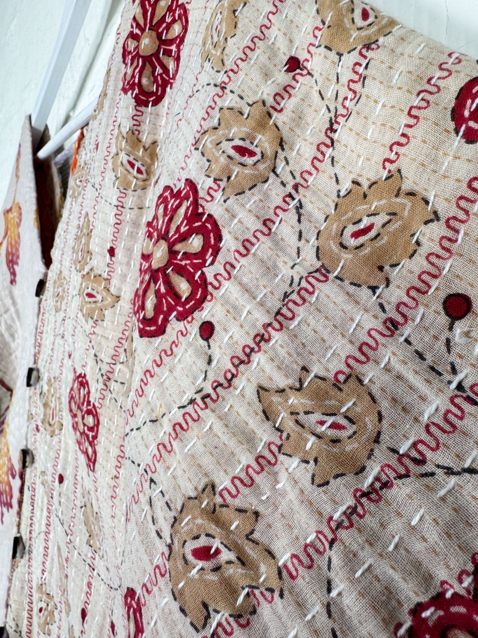 Close-up of a textured fabric with floral patterns in red and brown on a beige background.