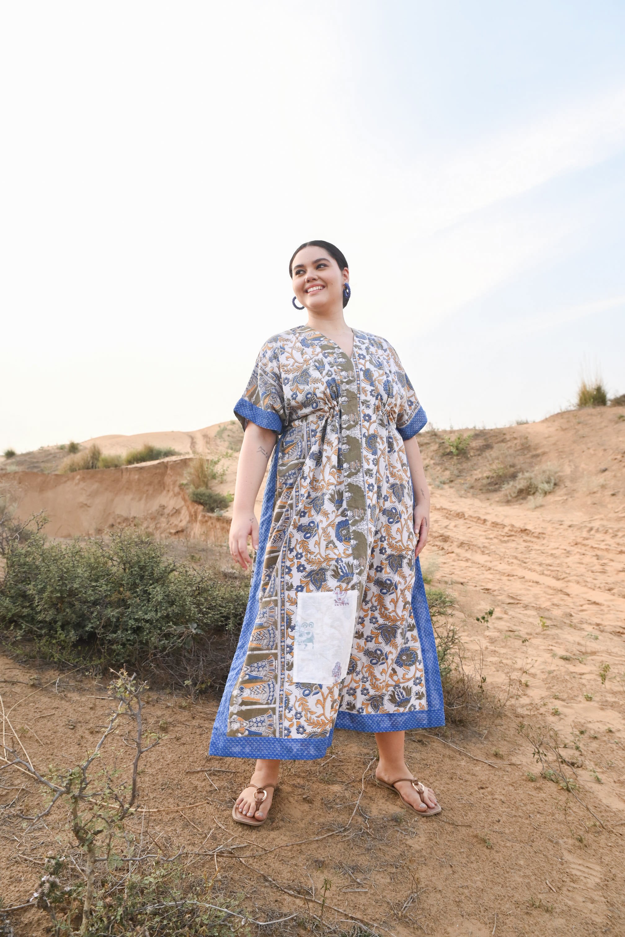 Woman wearing a floral Kaftan dress with floral accents standing in a desert landscape.