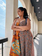 Woman standing on a balcony with a colorful dress, arms crossed- Love Protect Sustain